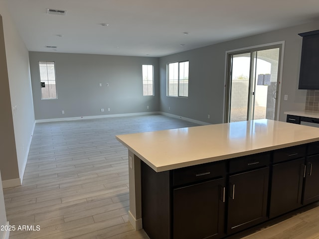 kitchen featuring visible vents, light wood-style flooring, a kitchen island, open floor plan, and light countertops