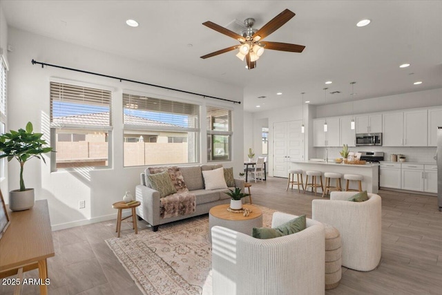 living area with light wood-type flooring, recessed lighting, baseboards, and ceiling fan