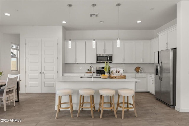 kitchen with visible vents, a sink, white cabinets, appliances with stainless steel finishes, and tasteful backsplash