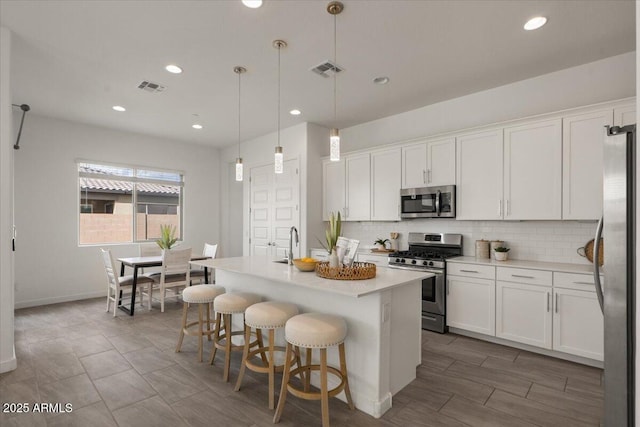 kitchen featuring visible vents, decorative backsplash, stainless steel appliances, white cabinetry, and a kitchen island with sink