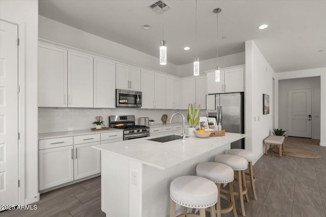 kitchen with visible vents, a breakfast bar area, decorative backsplash, stainless steel appliances, and a sink