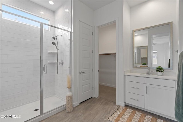 bathroom featuring a walk in closet, a stall shower, wood finished floors, baseboards, and vanity