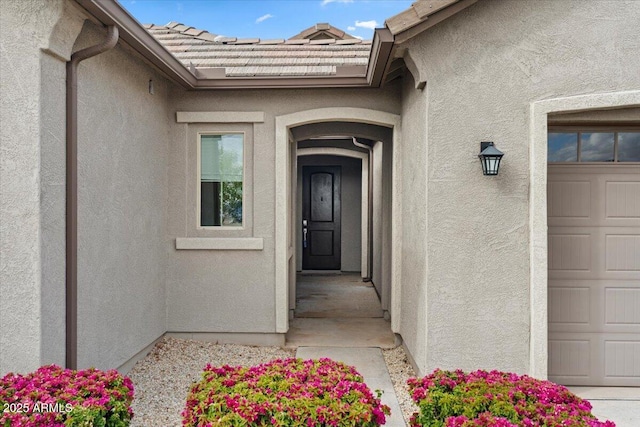 doorway to property with a tile roof, a garage, and stucco siding