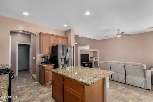 kitchen featuring visible vents, a center island, arched walkways, stainless steel fridge with ice dispenser, and black range with gas stovetop