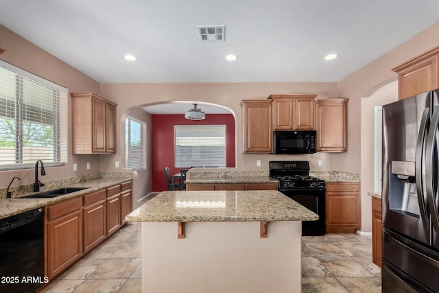 kitchen with visible vents, arched walkways, a center island, a sink, and black appliances