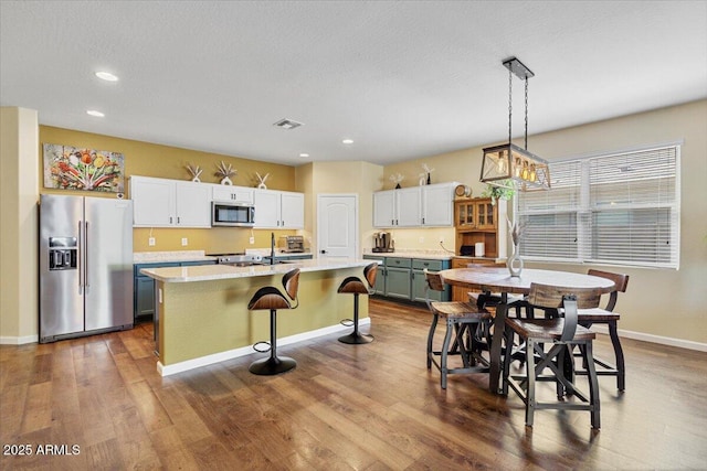 kitchen featuring baseboards, dark wood-style floors, light countertops, a kitchen island with sink, and stainless steel appliances