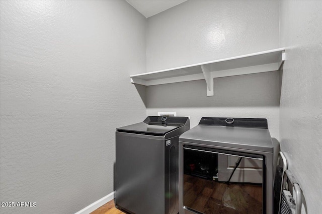 washroom featuring laundry area, wood finished floors, a textured wall, baseboards, and washing machine and dryer