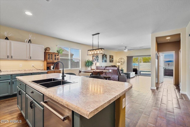 kitchen with stainless steel dishwasher, wood finished floors, light countertops, a sink, and decorative light fixtures