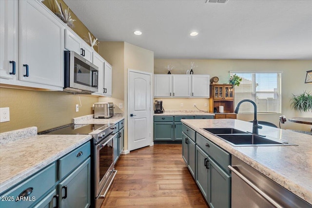 kitchen with light countertops, white cabinets, dark wood-type flooring, appliances with stainless steel finishes, and a sink