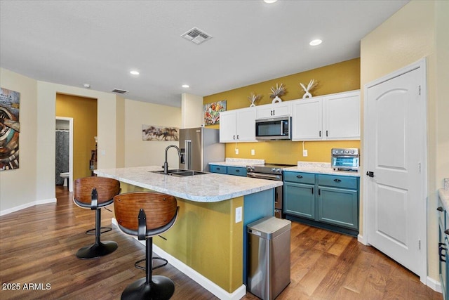 kitchen with dark wood-style floors, blue cabinetry, visible vents, stainless steel appliances, and a sink