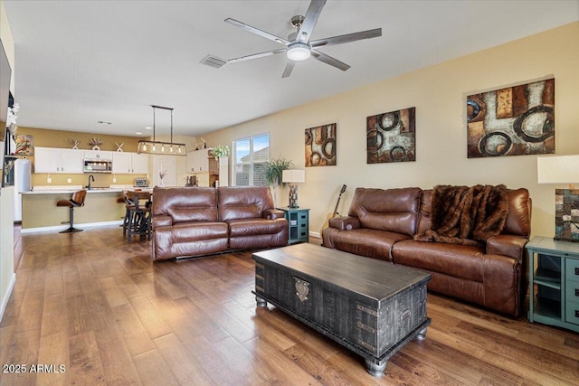 living room featuring visible vents, baseboards, wood finished floors, and ceiling fan