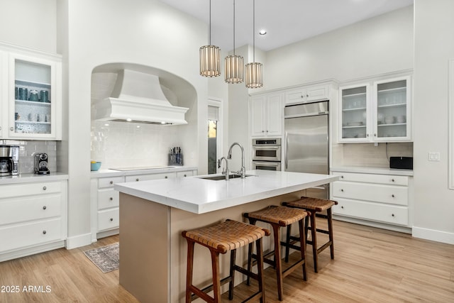 kitchen featuring a sink, light wood-style floors, light countertops, and premium range hood