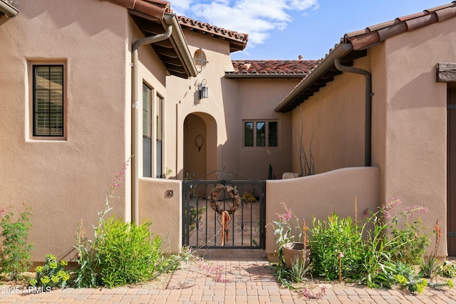 doorway to property featuring a tile roof, a gate, and stucco siding