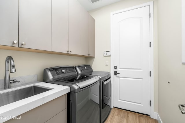 laundry room with light wood finished floors, cabinet space, a sink, and washing machine and clothes dryer