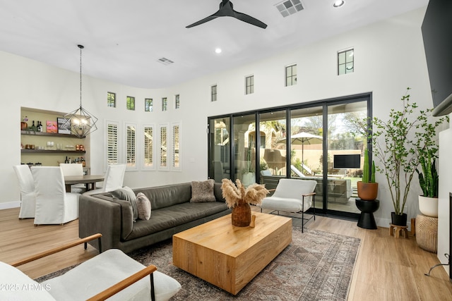 living area featuring visible vents, light wood-style flooring, ceiling fan with notable chandelier, and baseboards