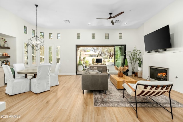 living room with a glass covered fireplace, ceiling fan with notable chandelier, visible vents, and light wood-type flooring