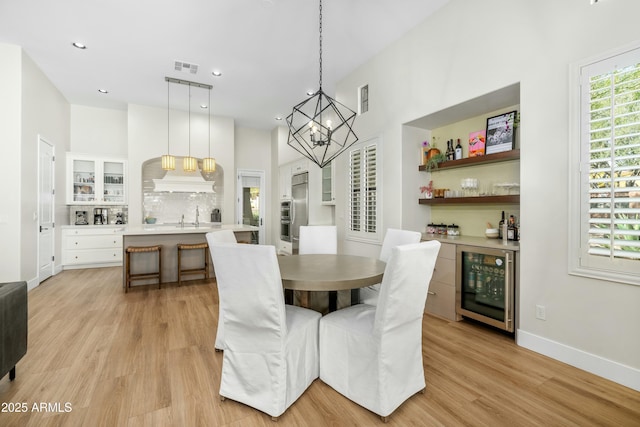 dining room with visible vents, baseboards, a bar, wine cooler, and light wood-style floors