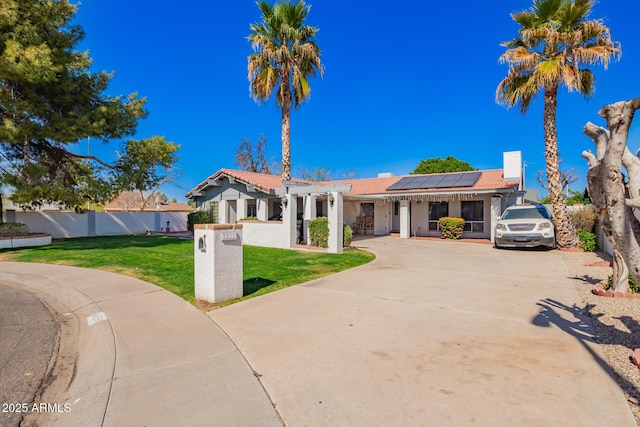 view of front of property with driveway, fence, a front lawn, and solar panels