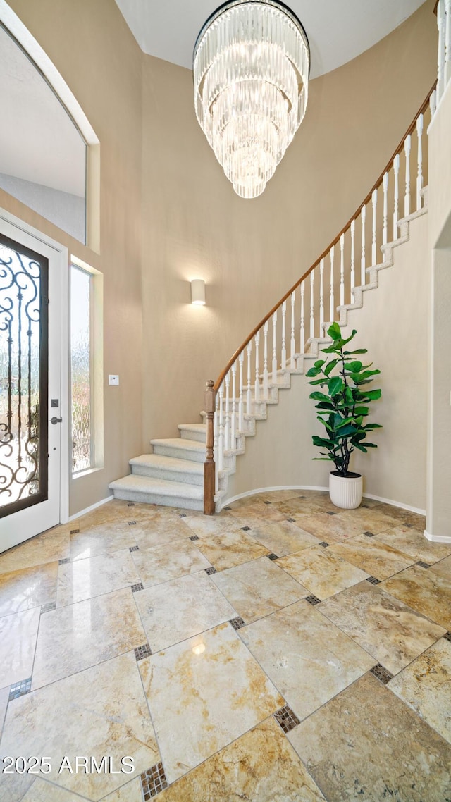 foyer with baseboards, a high ceiling, a chandelier, and stairs