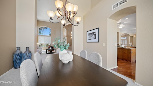 dining room with visible vents, ceiling fan with notable chandelier, wood finished floors, arched walkways, and baseboards