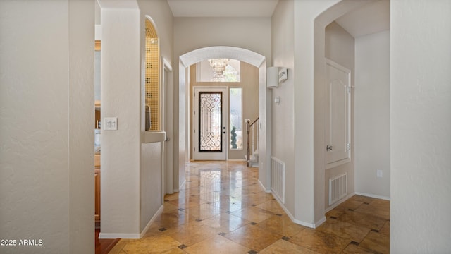 foyer entrance with visible vents, arched walkways, and baseboards