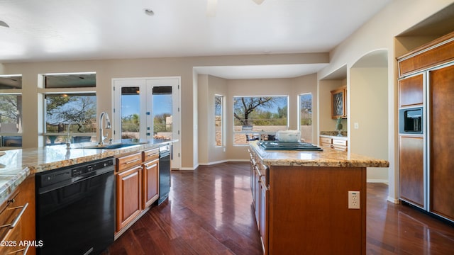 kitchen with a sink, light stone counters, dark wood-style floors, a center island, and dishwasher