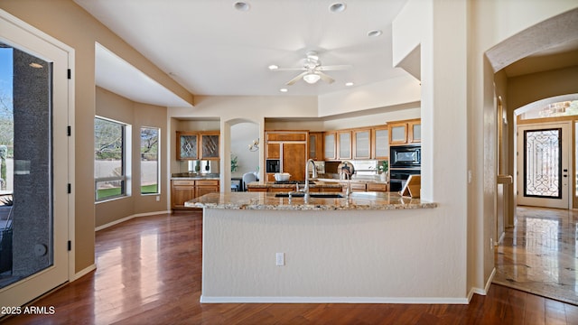 kitchen with black appliances, a sink, arched walkways, brown cabinetry, and dark wood-style flooring