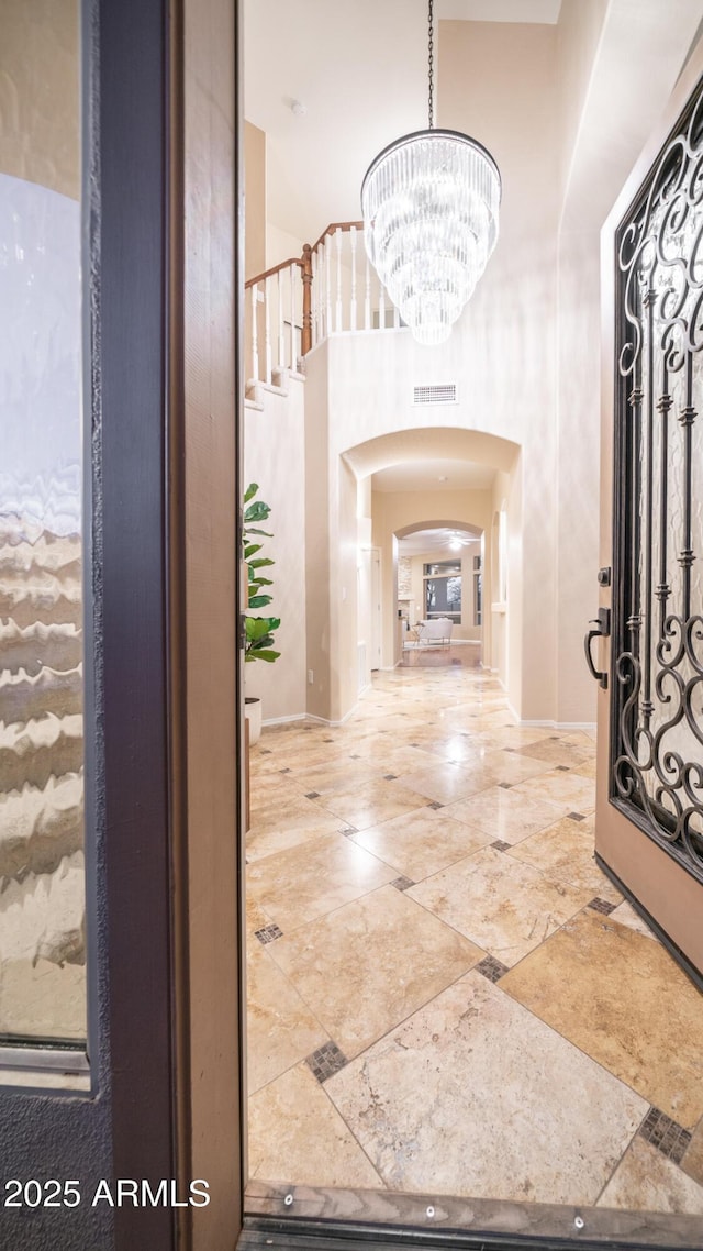 entrance foyer with visible vents, a notable chandelier, arched walkways, baseboards, and a towering ceiling