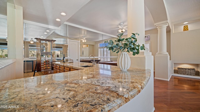 kitchen featuring a sink, wood finished floors, light stone countertops, ceiling fan, and ornate columns