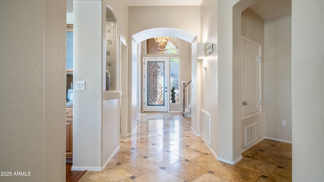 entryway featuring visible vents, arched walkways, baseboards, and an inviting chandelier