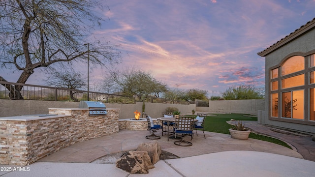 patio terrace at dusk featuring area for grilling, a fenced backyard, and a fire pit