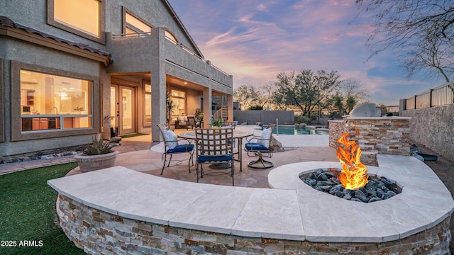 patio terrace at dusk featuring a fenced in pool, a fire pit, area for grilling, and a fenced backyard