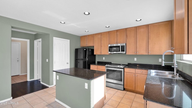 kitchen with a center island, dark stone counters, sink, light tile patterned floors, and appliances with stainless steel finishes