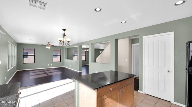 kitchen featuring dark stone countertops, light tile patterned flooring, ceiling fan with notable chandelier, and a kitchen island