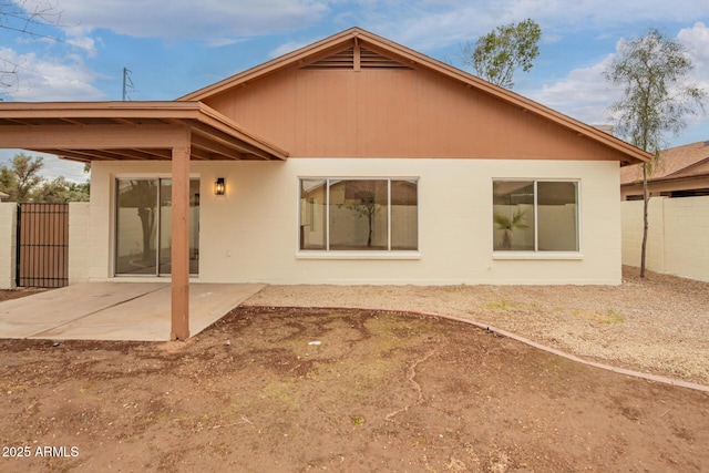 rear view of house with a patio area, concrete block siding, and fence