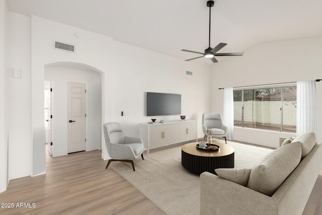 living room featuring visible vents, ceiling fan, light wood-type flooring, lofted ceiling, and arched walkways