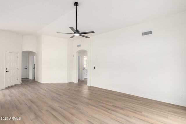 empty room featuring baseboards, visible vents, light wood-style flooring, arched walkways, and ceiling fan