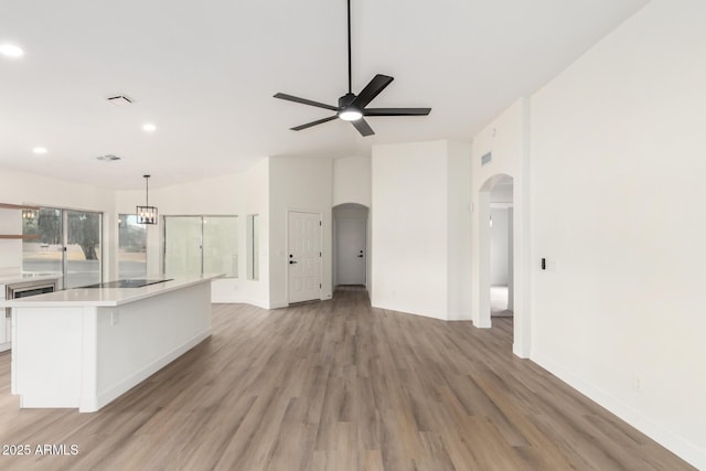 unfurnished living room featuring baseboards, arched walkways, light wood finished floors, and ceiling fan