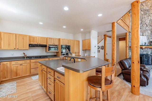 kitchen featuring a center island with sink, sink, gas stovetop, light wood-type flooring, and a fireplace