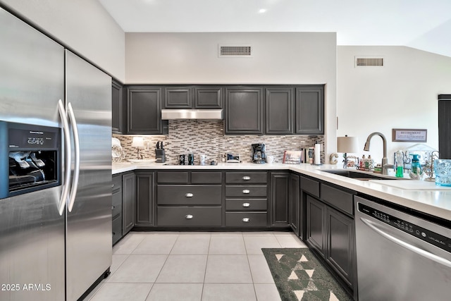 kitchen with backsplash, sink, vaulted ceiling, light tile patterned floors, and appliances with stainless steel finishes