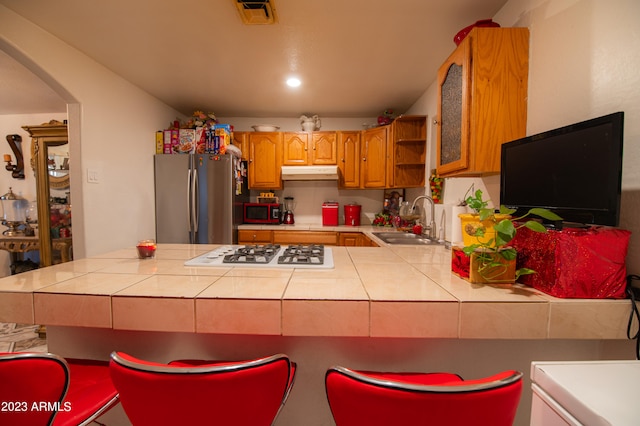 kitchen with white gas cooktop, tile countertops, stainless steel fridge, and sink