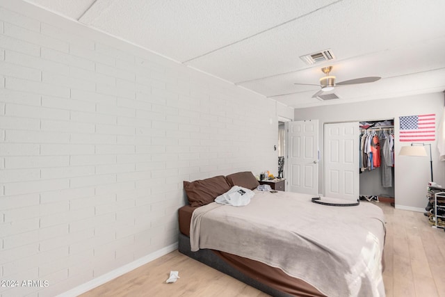 bedroom featuring light hardwood / wood-style flooring, a textured ceiling, brick wall, and a closet