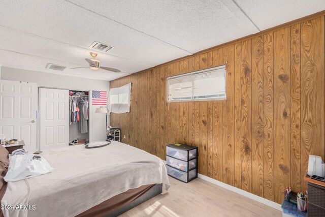 bedroom featuring a closet, light hardwood / wood-style floors, wood walls, and ceiling fan