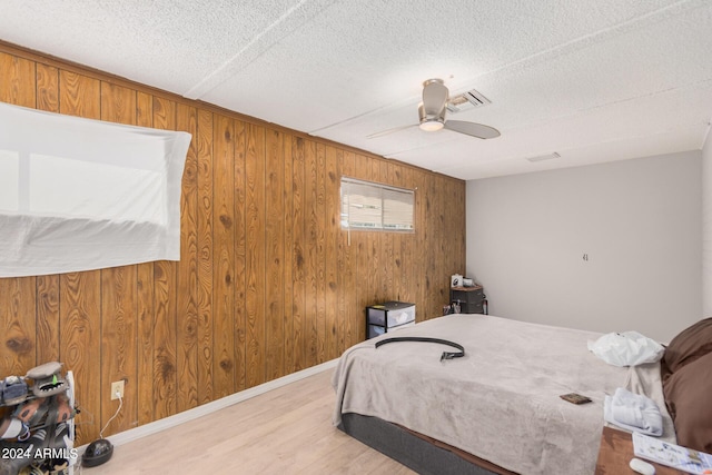 bedroom with wood walls, ceiling fan, light wood-type flooring, and a textured ceiling