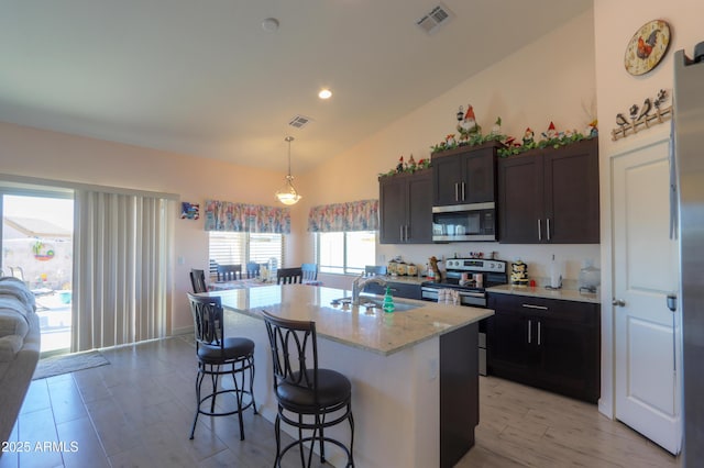 kitchen with decorative light fixtures, stainless steel appliances, a sink, visible vents, and a center island with sink