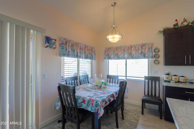 dining room with a healthy amount of sunlight, light wood finished floors, baseboards, and vaulted ceiling