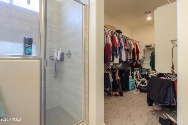 full bathroom featuring a spacious closet, wood finished floors, a shower stall, and visible vents