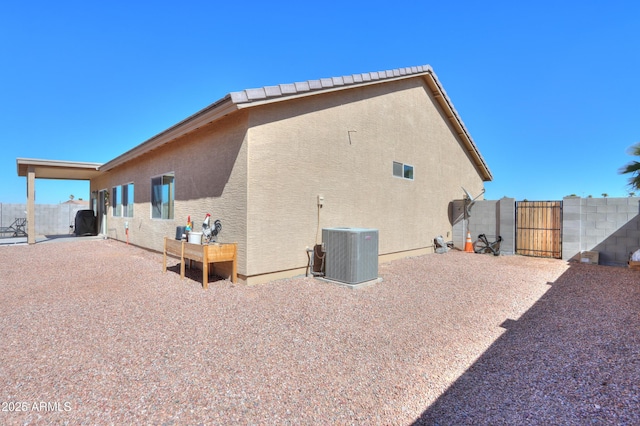 view of side of home featuring a gate, stucco siding, fence, and central AC unit