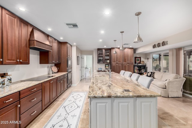 kitchen featuring black electric stovetop, sink, hanging light fixtures, a large island, and custom range hood