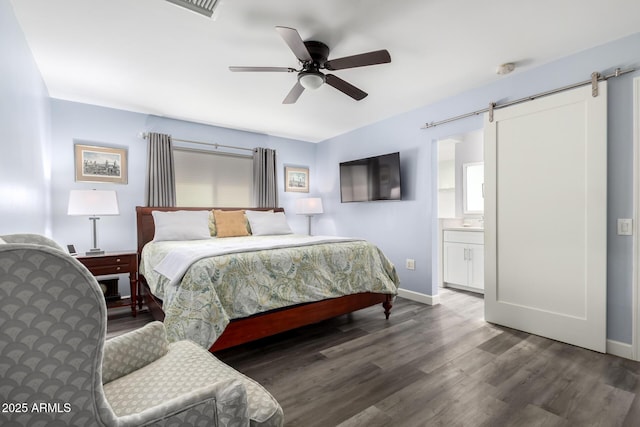 bedroom with connected bathroom, a barn door, ceiling fan, and dark hardwood / wood-style flooring